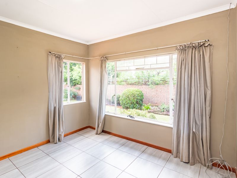 A bright, empty living room featuring neutral wall tones, tiled flooring, and large steel-framed windows overlooking the garden.