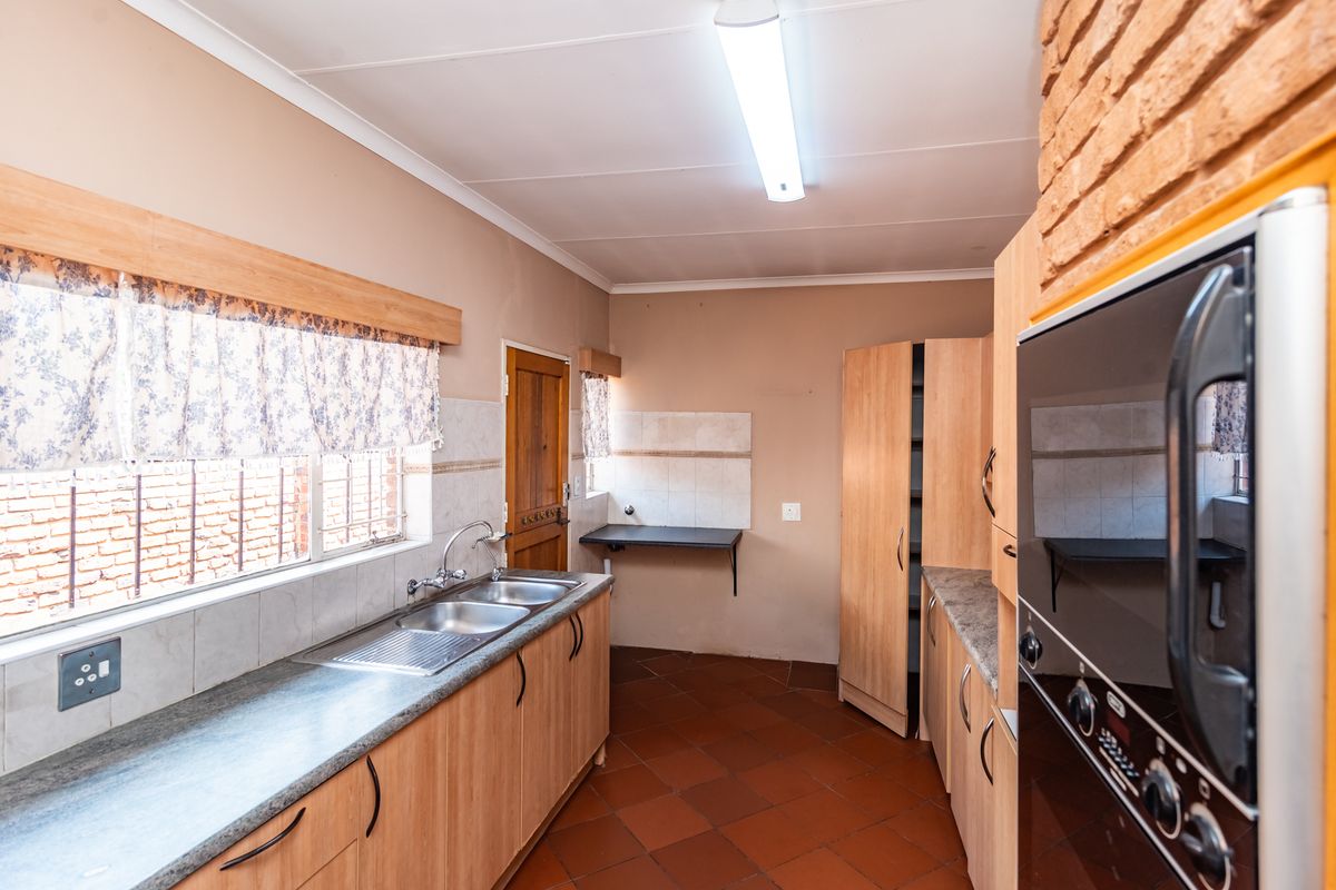 A functional kitchen featuring laminate cabinetry, double stainless steel sink, built-in oven, and terracotta floor tiles with an exposed brick accent wall.