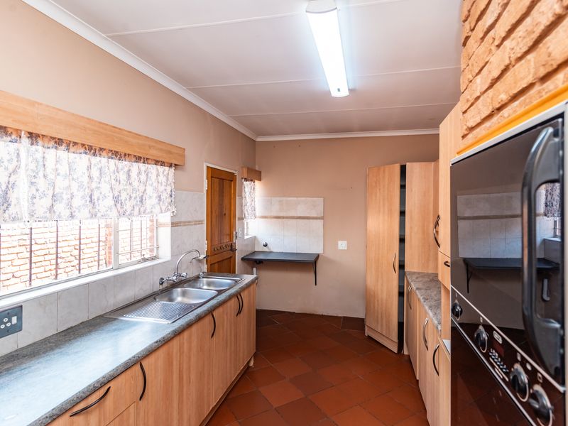 A functional kitchen featuring laminate cabinetry, double stainless steel sink, built-in oven, and terracotta floor tiles with an exposed brick accent wall.