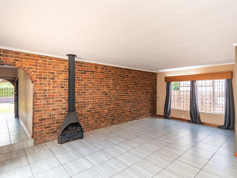 Spacious living room featuring an exposed brick wall, a freestanding fireplace, and neutral tiled flooring, offering a versatile blank canvas for interior design.