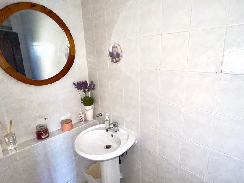 A compact bathroom featuring a pedestal basin with a mixer tap and fully tiled walls.