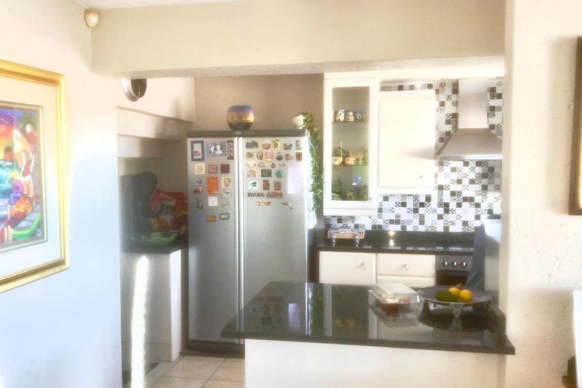 A compact kitchen featuring granite countertops, a stainless steel extractor fan, and patterned tiled backsplash with built-in cabinetry.