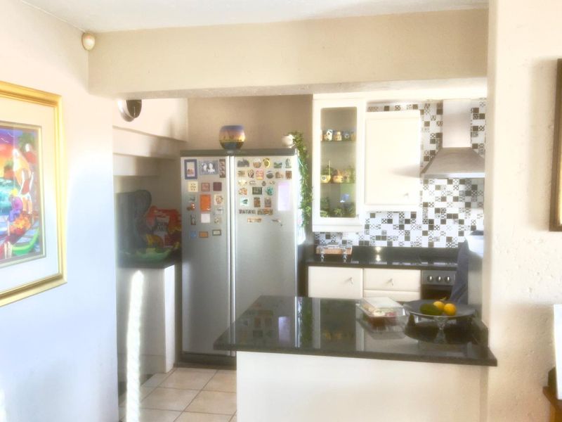 A compact kitchen featuring granite countertops, a stainless steel extractor fan, and patterned tiled backsplash with built-in cabinetry.