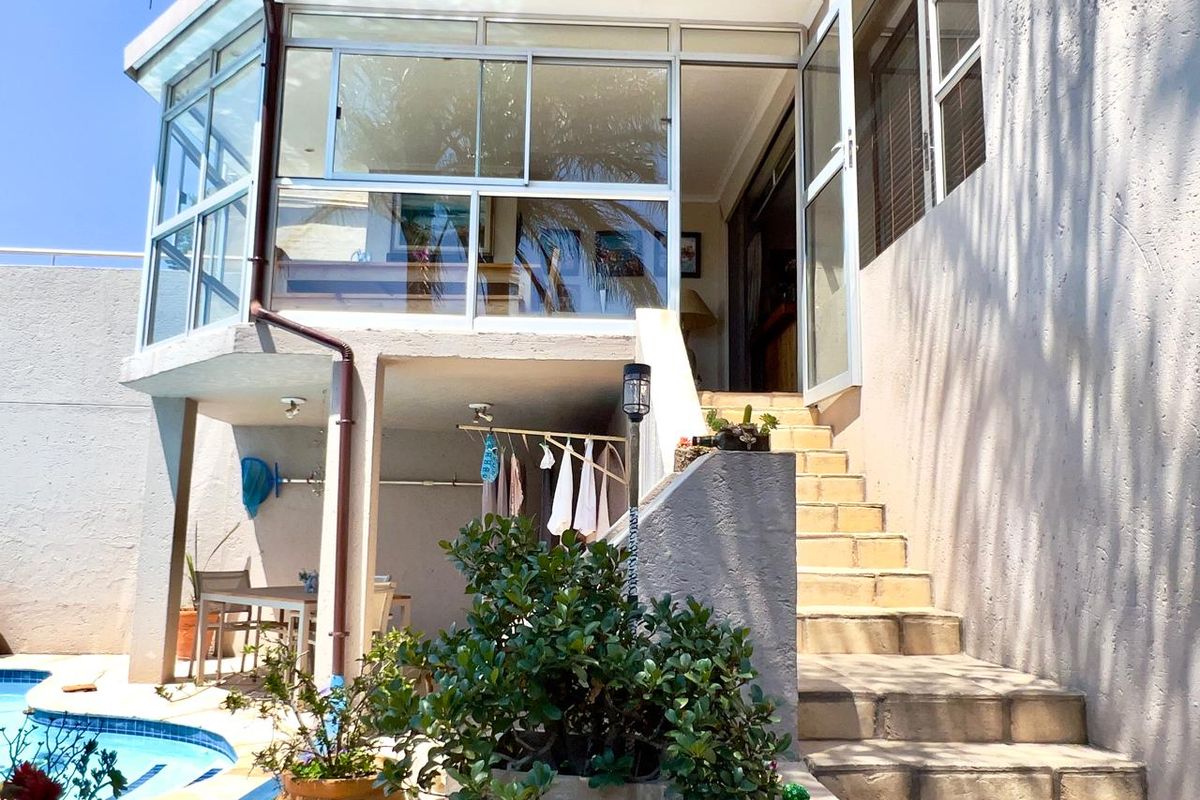 Rear exterior view featuring a swimming pool, concrete staircase leading to an enclosed patio, and established garden elements.