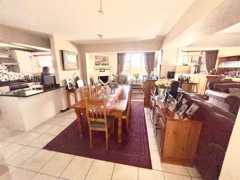 An open-plan living and dining area featuring tiled flooring, a fireplace, and an adjacent kitchen with built-in cabinetry and appliances.