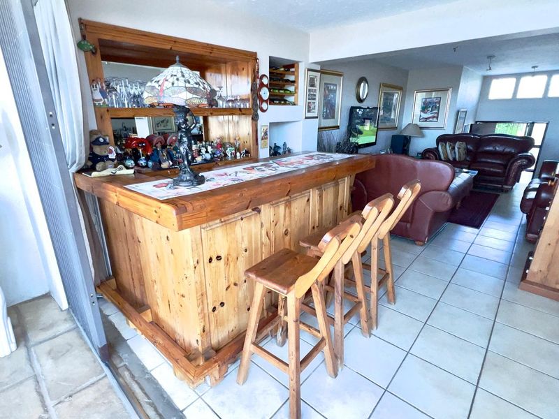 A dedicated bar area featuring a built-in wooden counter with mirrored shelving, seamlessly integrated into the open-plan living space with tiled flooring.