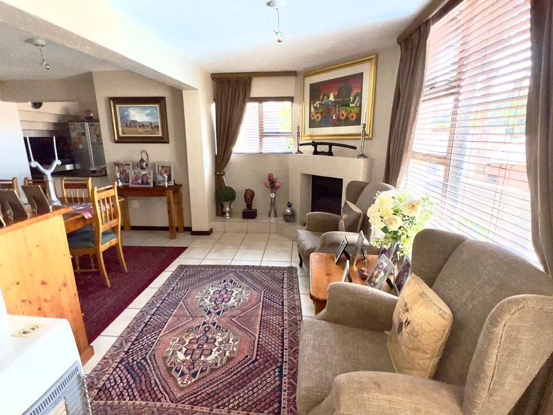 Open-plan living and dining area featuring tiled flooring, a built-in fireplace, and large windows with venetian blinds, creating a bright and functional living space.