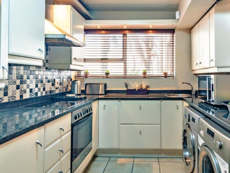 A functional kitchen featuring built-in cabinetry, granite countertops, integrated oven, and a tiled backsplash, with space for laundry appliances.