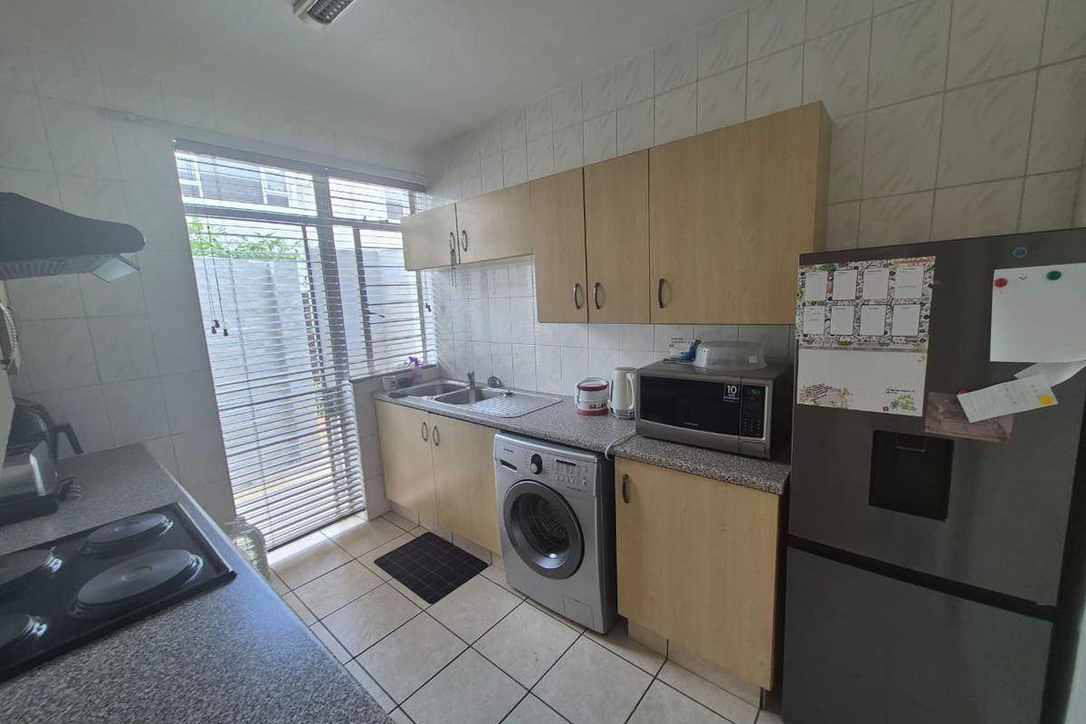 Functional kitchen featuring laminate cabinetry, granite-look countertops, tiled splashbacks, and integrated laundry plumbing, offering a practical layout with natural light.