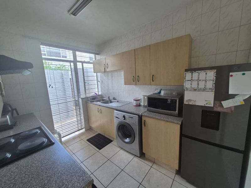 Functional kitchen featuring laminate cabinetry, granite-look countertops, tiled splashbacks, and integrated laundry plumbing, offering a practical layout with natural light.