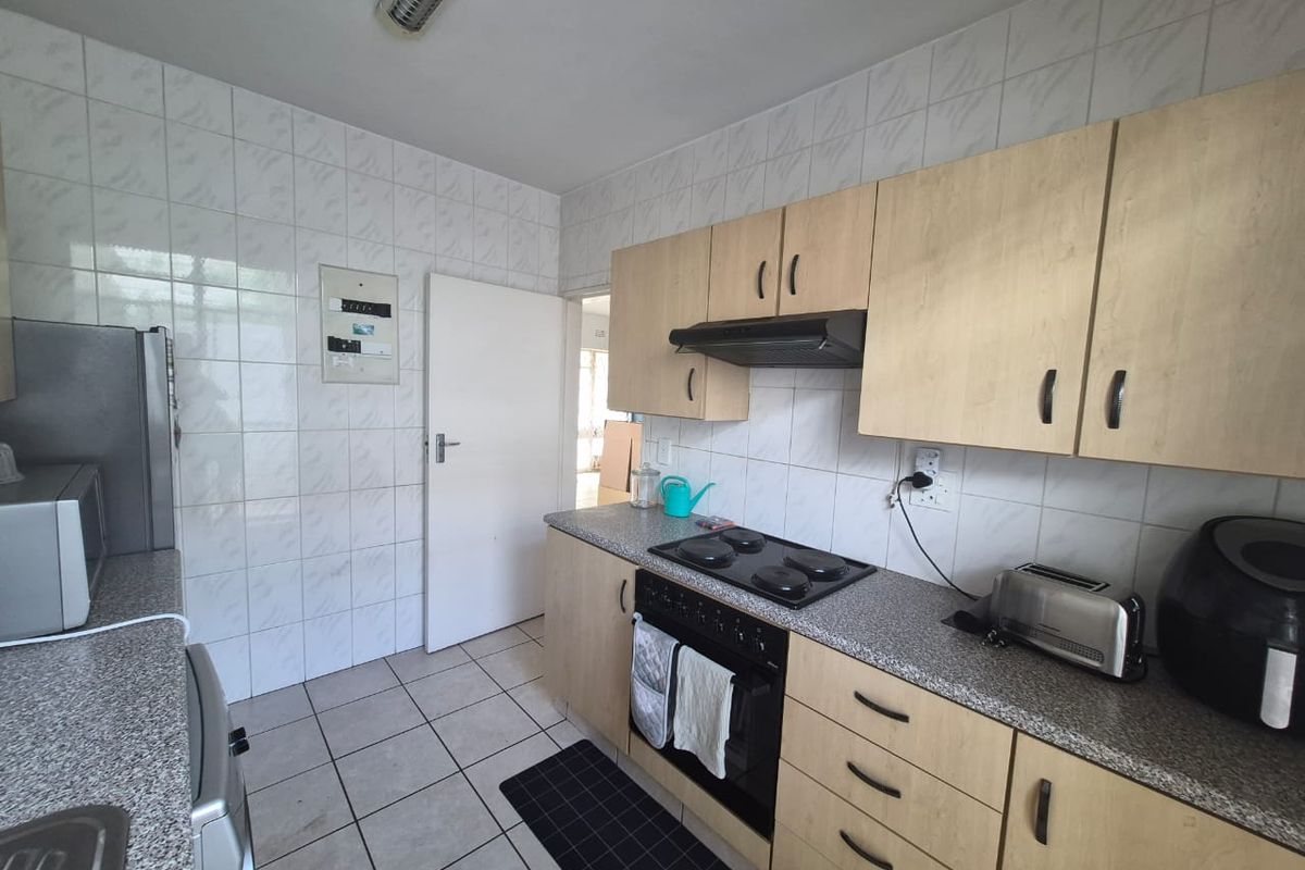 Functional kitchen featuring light wood-finish cabinetry, laminate countertops, built-in oven with electric hob, and full-height wall tiling.