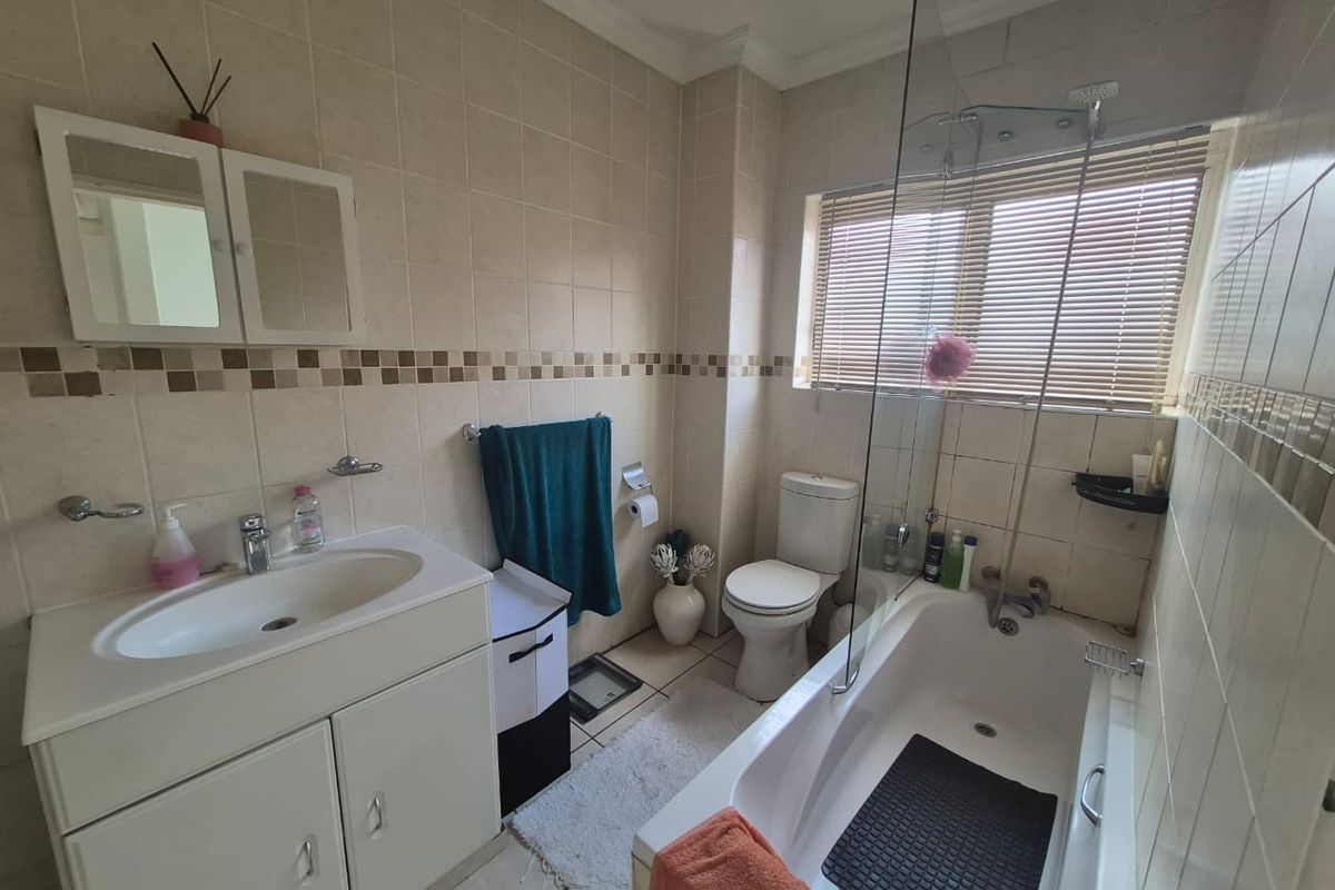 A functional bathroom featuring a vanity with basin, a bathtub with a glass shower screen, and neutral wall tiling.
