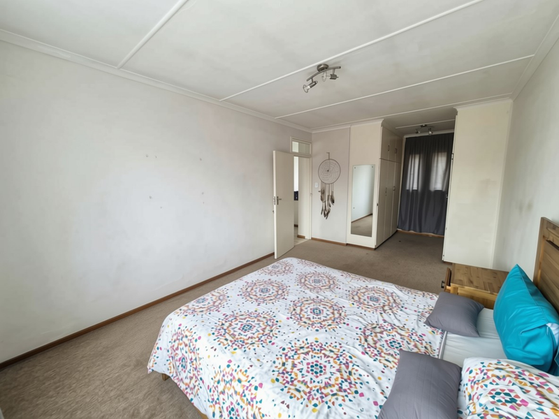 A bedroom featuring built-in cupboards with a mirrored door, carpeted flooring, and neutral wall finishes, offering a functional space with potential for cosmetic updates.