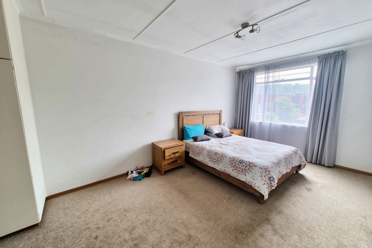 A spacious bedroom featuring built-in wardrobes, carpeted flooring, and large windows with curtains, offering a blank canvas for potential interior updates.