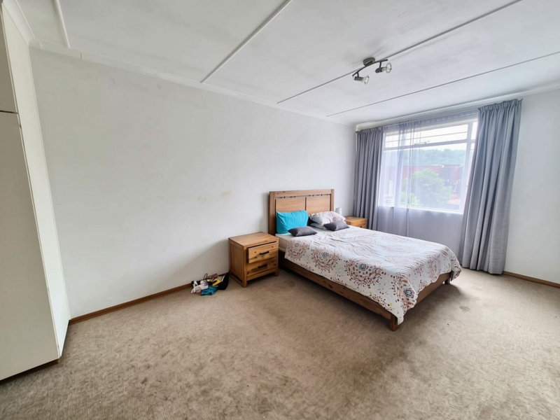 A spacious bedroom featuring built-in wardrobes, carpeted flooring, and large windows with curtains, offering a blank canvas for potential interior updates.