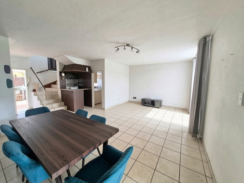 Spacious open-plan living and dining area featuring tiled flooring, a built-in bar, and a staircase leading to the upper level.