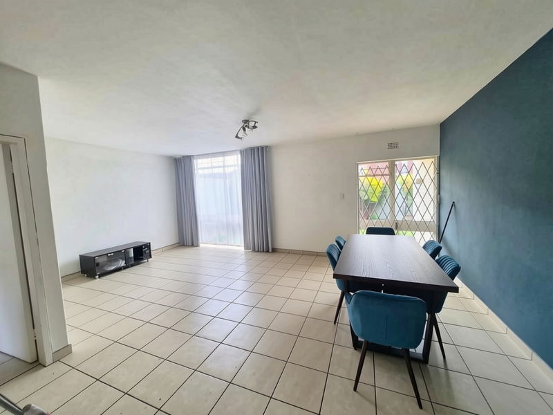 Spacious open-plan living and dining area featuring neutral tiled flooring, a feature wall, and direct access to the exterior through a security gate.