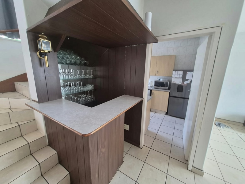 A built-in wooden bar area adjacent to a staircase, featuring tiled flooring and a view into the adjoining kitchen space.