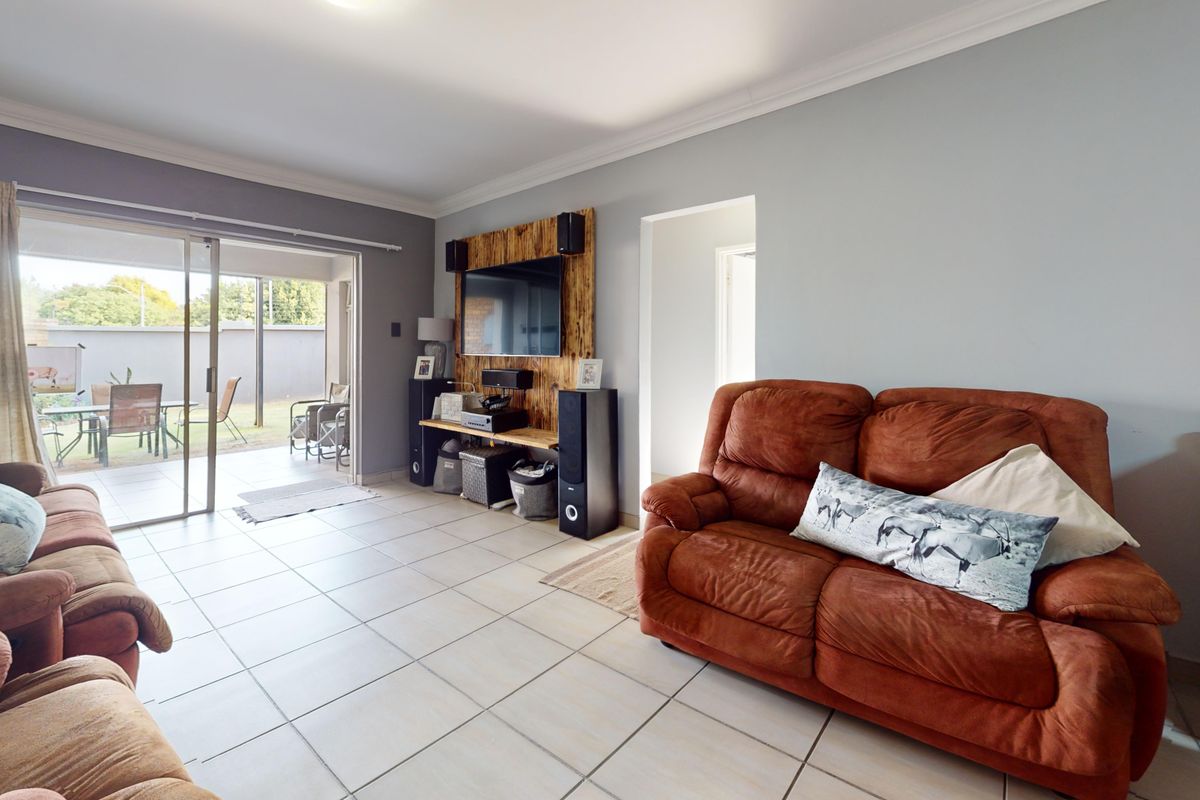 Spacious living room featuring tiled flooring, a built-in media wall, and large sliding glass doors providing direct access to the outdoor patio area.