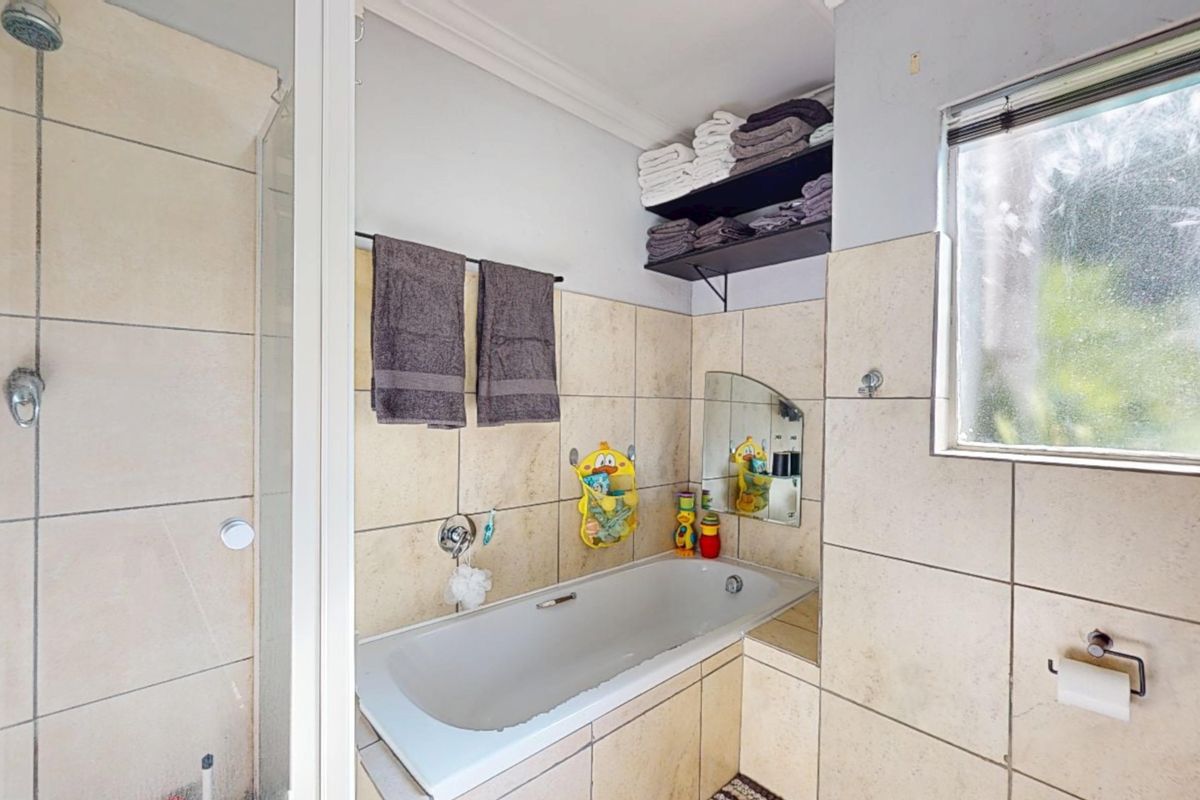 A functional bathroom featuring a built-in bathtub, shower head, tiled walls, and built-in shelving, providing a practical space with potential for cosmetic updates.