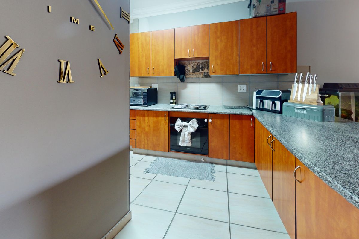 Functional kitchen featuring wood-look laminate cabinetry, granite countertops, built-in oven, gas hob, and tiled flooring.