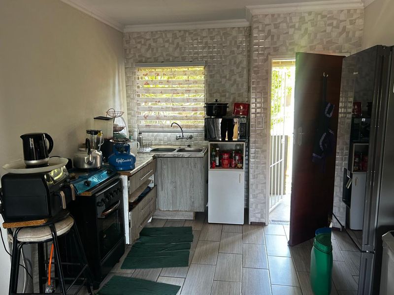 A functional kitchen featuring tiled flooring, a double sink, and built-in cabinetry with a tiled backsplash, providing direct access to an outdoor area.