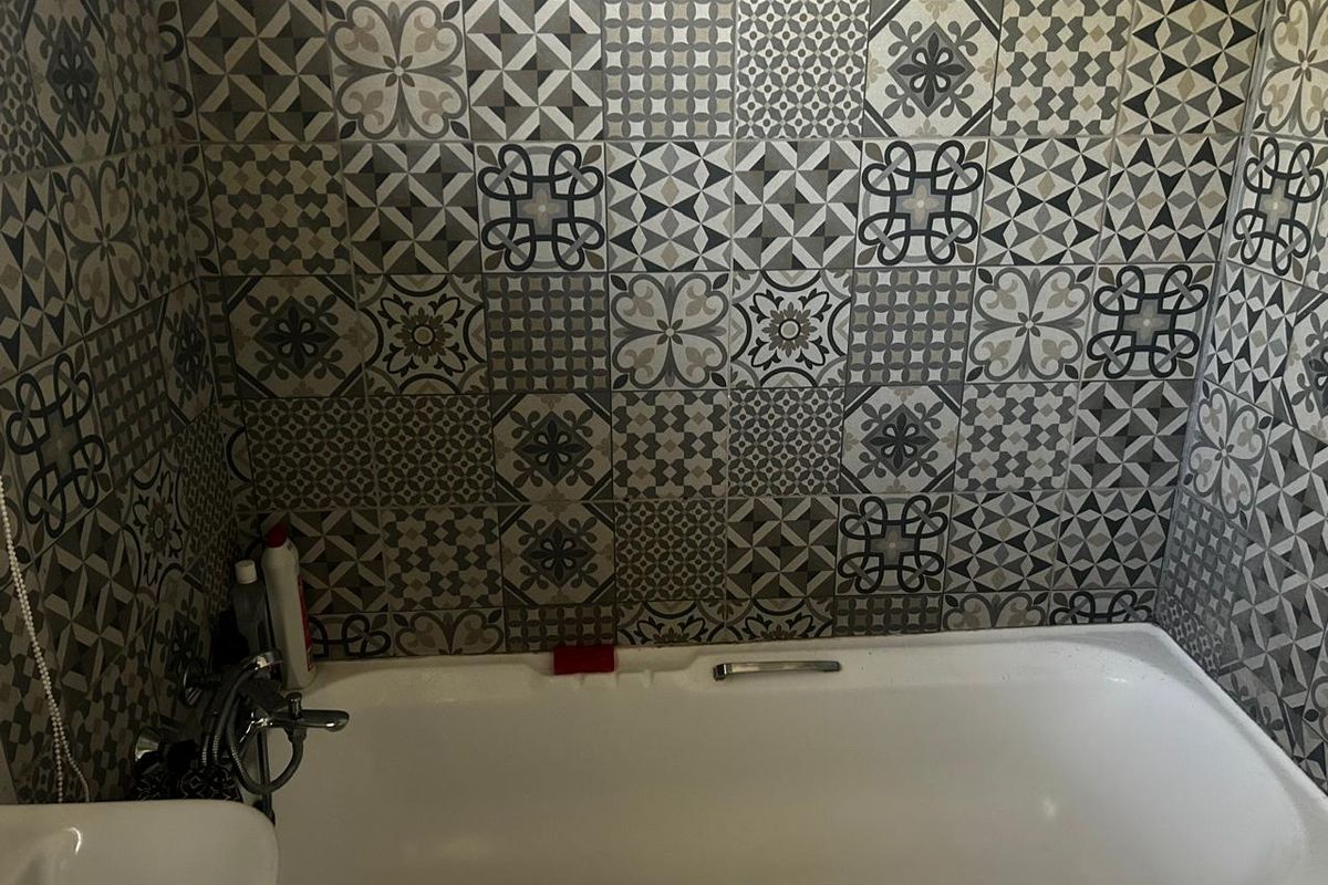A bathroom featuring a bathtub with a chrome faucet and decorative patterned wall tiling.