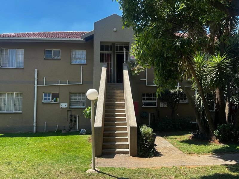 Front exterior view of an apartment building featuring a central concrete staircase, tiled roof, and paved walkway access.