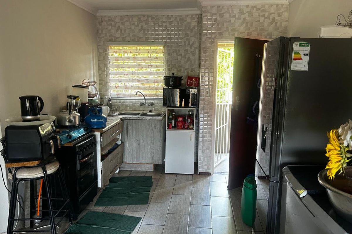 A functional kitchen featuring tiled flooring, a double sink, and built-in cabinetry with a decorative tiled backsplash and direct access to an outdoor area.