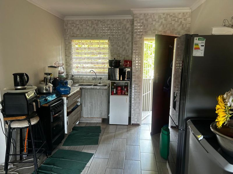 A functional kitchen featuring tiled flooring, a double sink, and built-in cabinetry with a decorative tiled backsplash and direct access to an outdoor area.