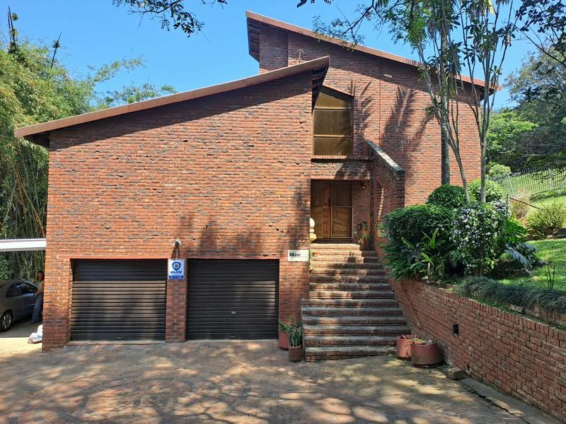 Front elevation of a multi-level brick house featuring a double garage, prominent staircase leading to the main entrance, and established garden surroundings.
