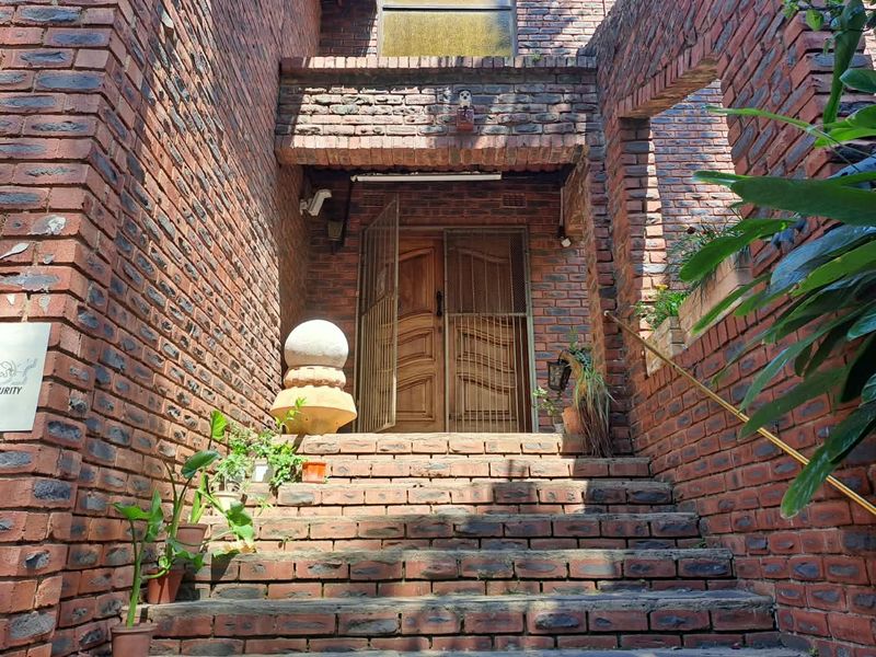 Front entrance featuring a brick staircase leading to a wooden front door with a security gate and metal handrail.