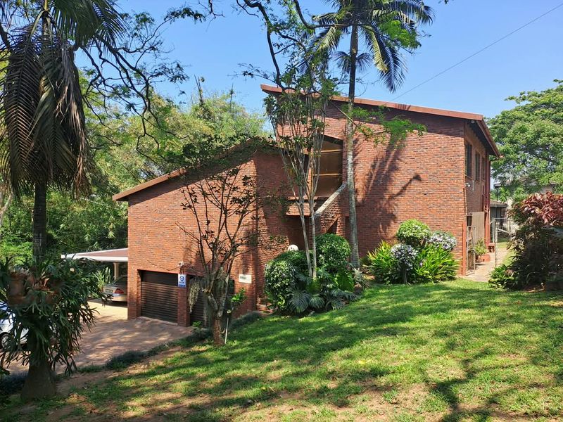 A multi-level face brick house featuring a double garage, paved driveway, and established garden surroundings.