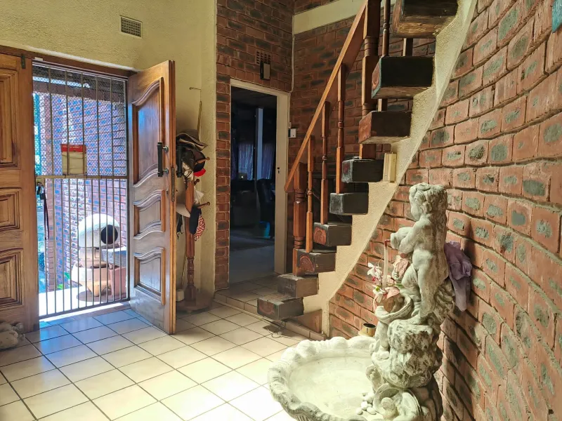 Entrance hall featuring exposed brick walls, ceramic tiled flooring, and a wooden staircase leading to the upper level.