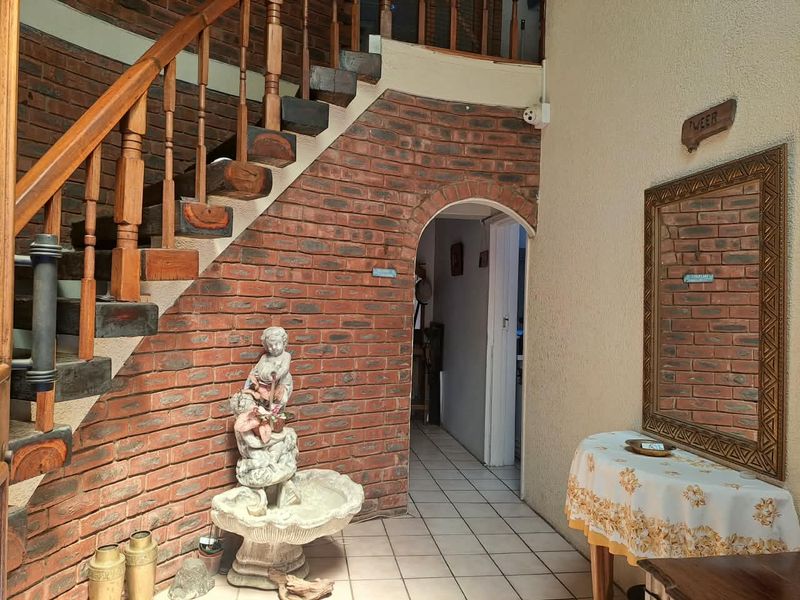 Entrance hall featuring an exposed brick feature wall, a wooden staircase, and tiled flooring leading through an arched doorway.