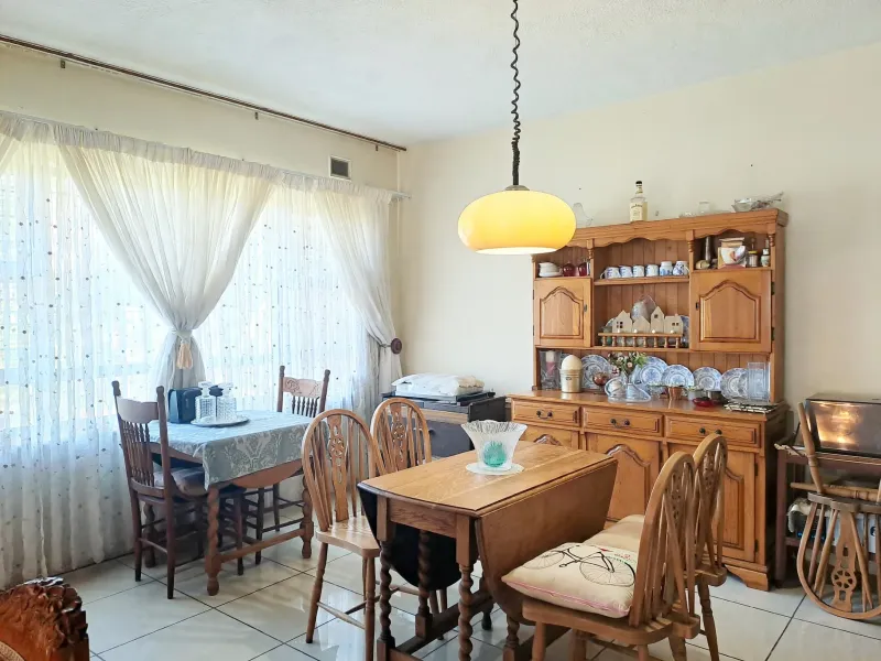 A dining room featuring tiled flooring, a large window with curtains, and a central pendant light fixture.