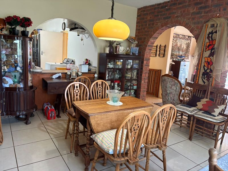 Dining area featuring ceramic floor tiles, an exposed brick archway, and a pass-through window connecting to the kitchen space.
