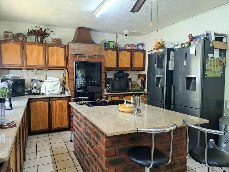 A functional kitchen featuring a central brick island with granite countertop, built-in oven, copper extractor hood, and traditional wooden cabinetry.