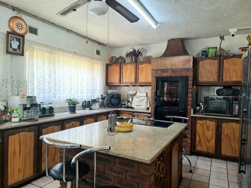 A spacious kitchen featuring a central brick island with granite countertop, custom copper range hood, built-in oven, and traditional wooden cabinetry.