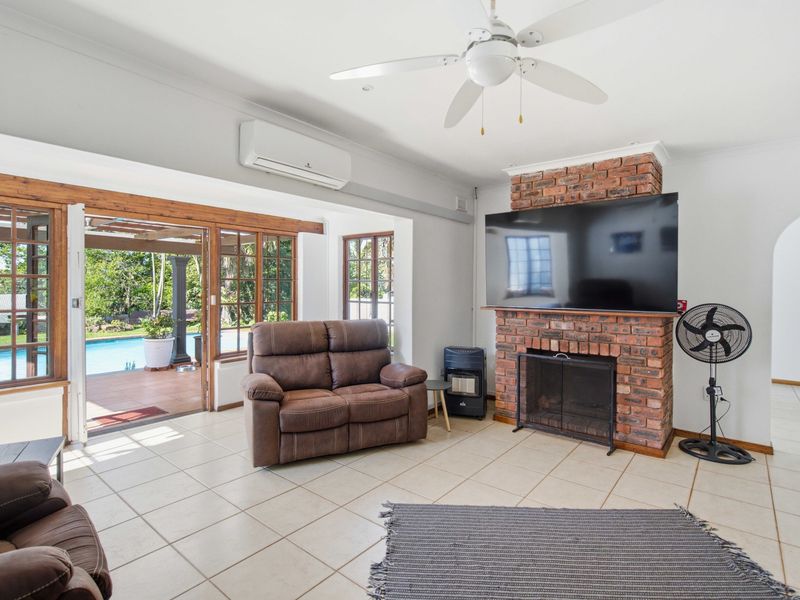 Spacious living room featuring an exposed brick fireplace, tiled flooring, and direct access to the outdoor patio and pool area through timber-framed sliding doors.