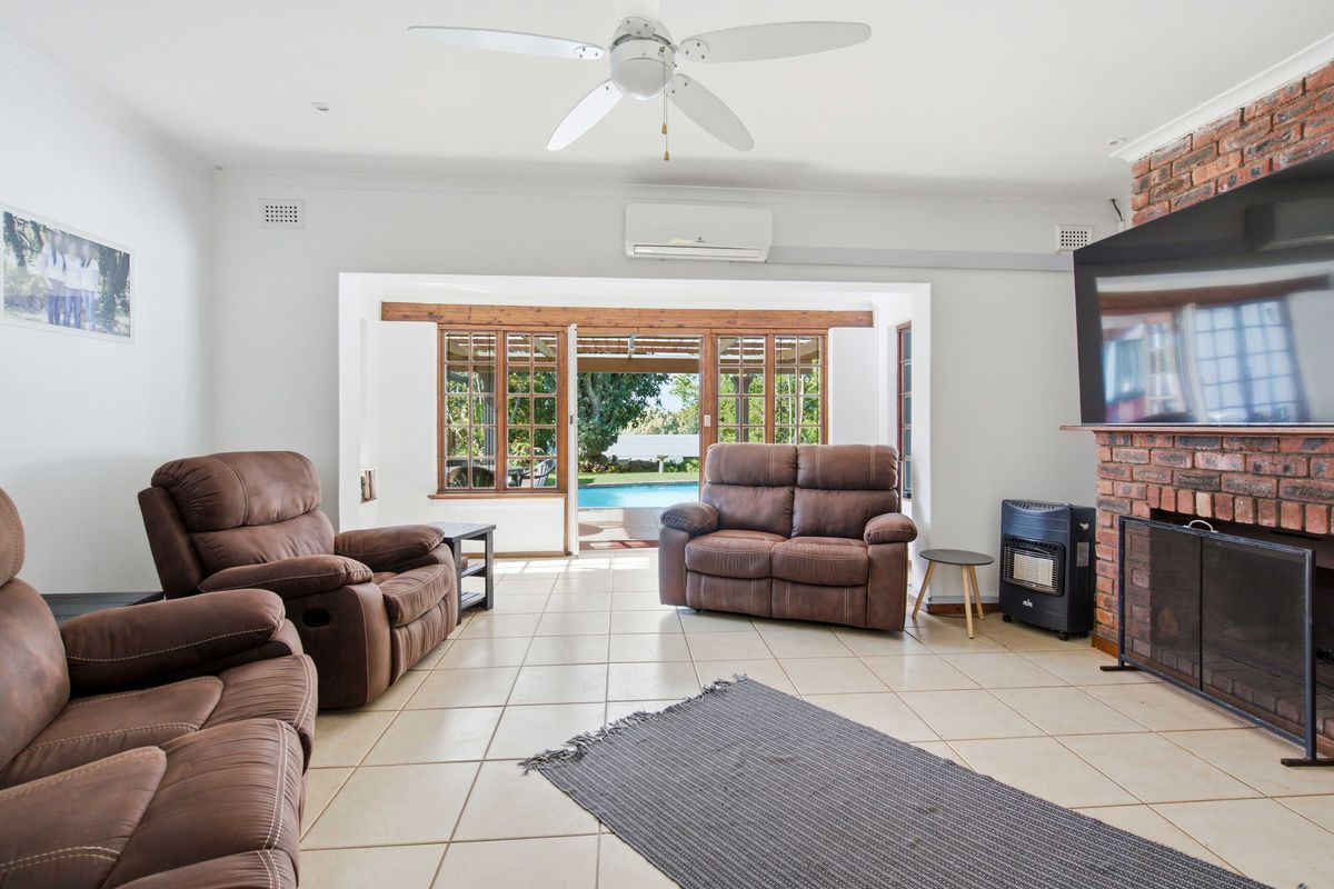 Spacious living room featuring tiled floors, an exposed brick fireplace, and direct access to the outdoor pool area through timber-framed glass doors.