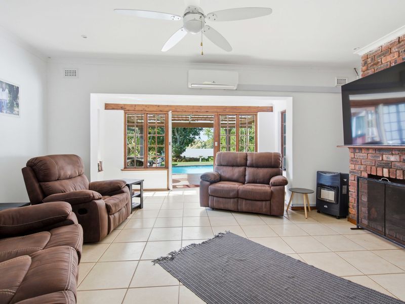 Spacious living room featuring tiled floors, an exposed brick fireplace, and direct access to the outdoor pool area through timber-framed glass doors.