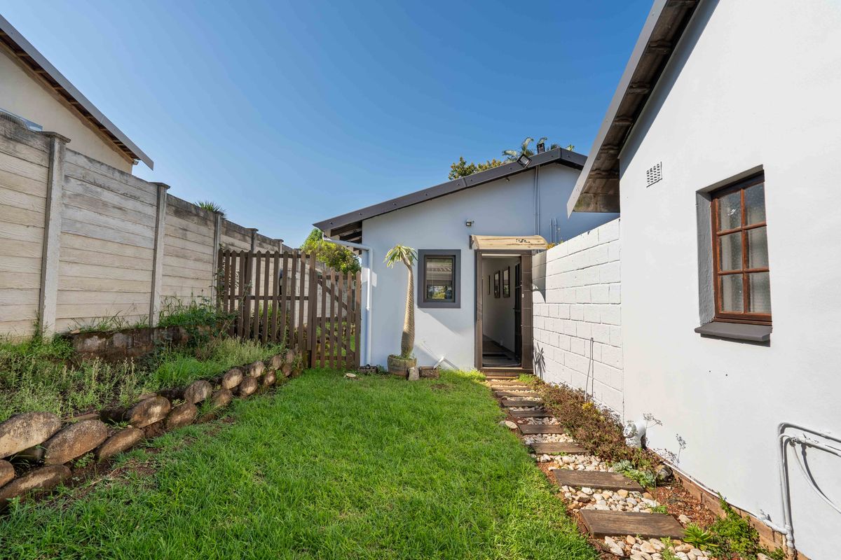A rear garden area featuring a stone retaining wall, a timber gate, and a stone-paved pathway leading to an exterior entrance.