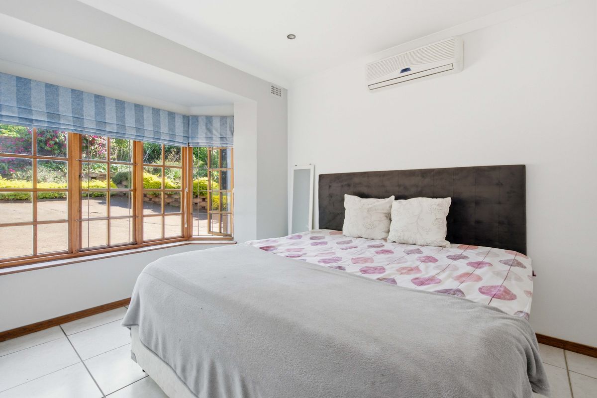 A bright bedroom featuring a large bay window, tiled flooring, and a wall-mounted split-system air conditioner.