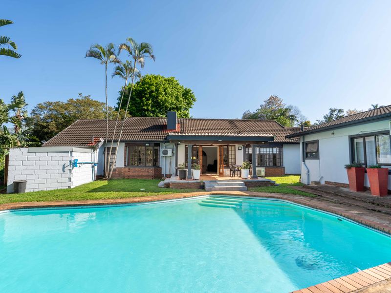 Rear view of the property featuring a swimming pool, covered patio area, and established garden surroundings.