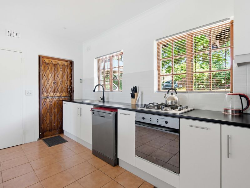 A functional kitchen featuring white cabinetry, dark countertops, a gas cooktop, built-in oven, and tiled flooring with direct access to an exterior security door.