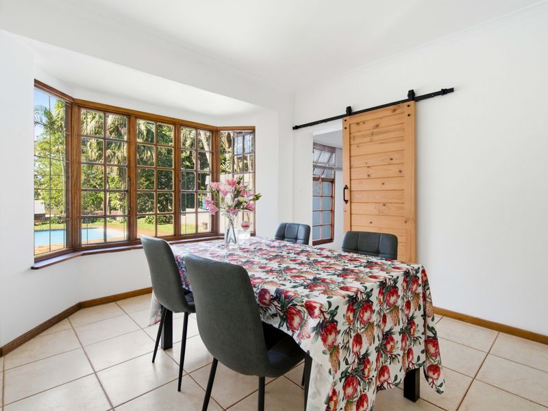 Bright dining room featuring a large bay window with garden views, tiled flooring, and a rustic timber sliding barn door.