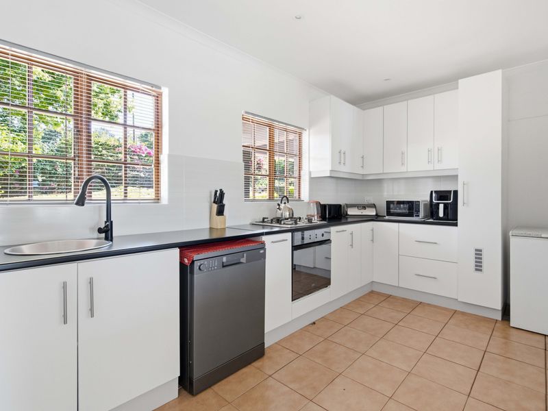 A clean, functional kitchen featuring white cabinetry, black countertops, built-in oven, gas hob, and tiled flooring with ample natural light from two windows.