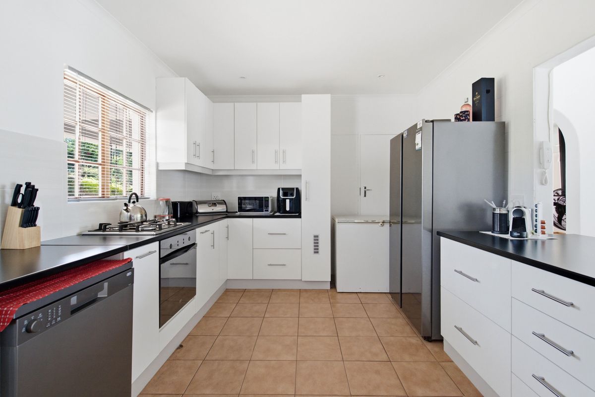 A functional kitchen featuring white cabinetry, dark laminate countertops, a gas hob, built-in oven, and tiled flooring with natural light from the window.