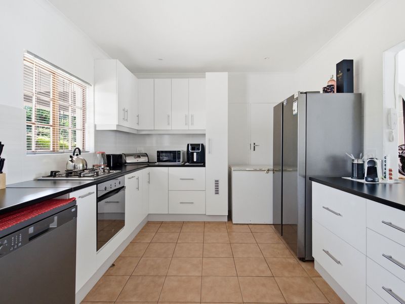A functional kitchen featuring white cabinetry, dark laminate countertops, a gas hob, built-in oven, and tiled flooring with natural light from the window.